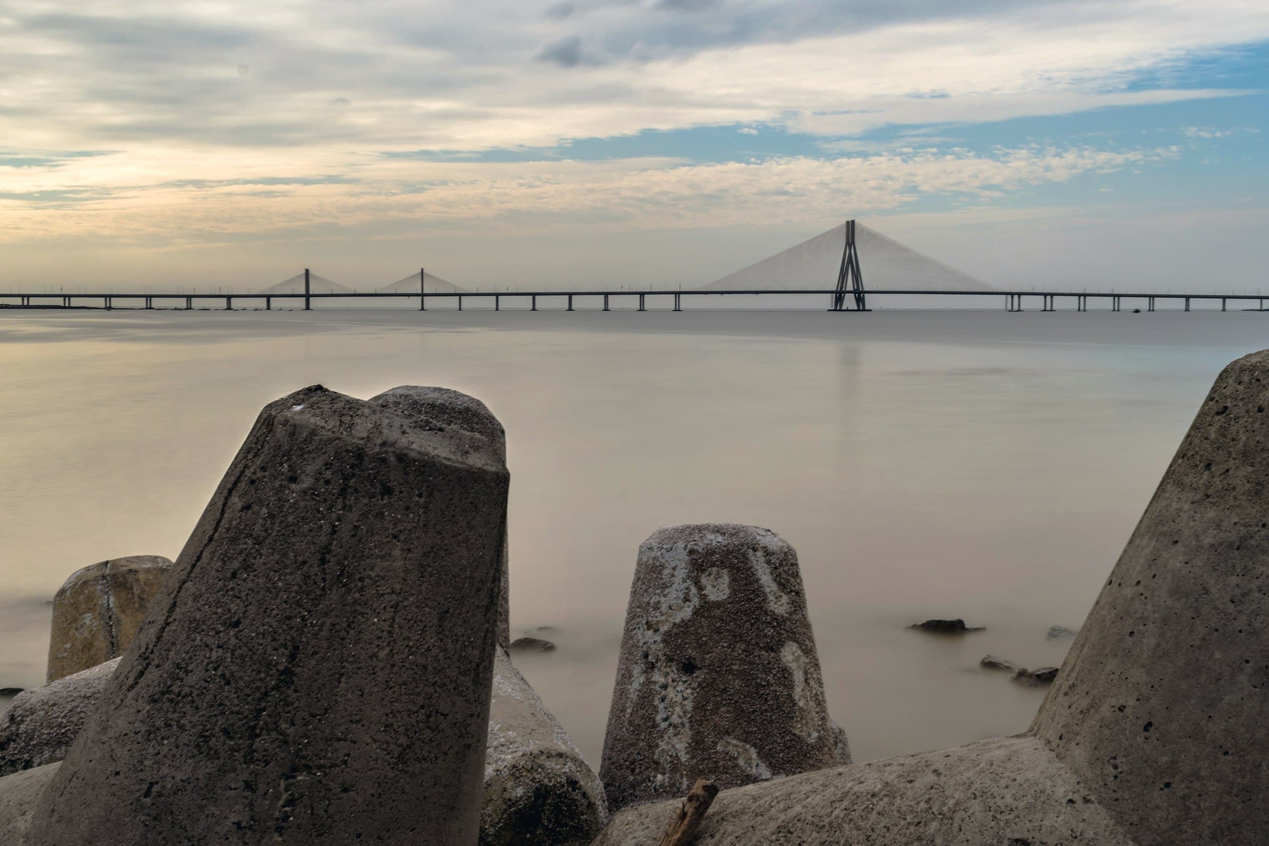 The Bandra–Worli Sea Link stretching across the bay at golden hour, seen from the rocks at the shore